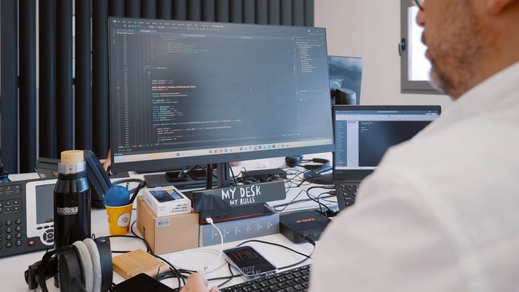 Posto de trabalho com código num monitor e ferramentas de gestão